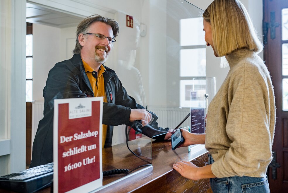 Kassierer begrüßt eine Besucherin an der Kasse